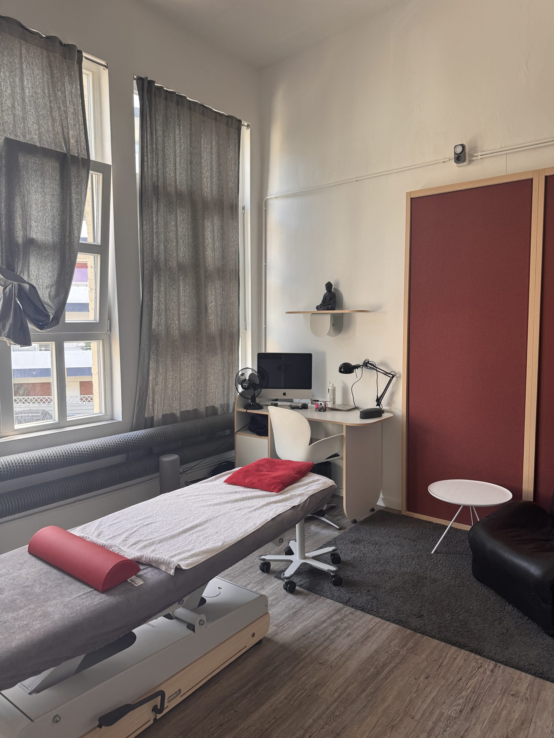 Heller Behandlungsraum mit Therapieliege und großen Fenstern
